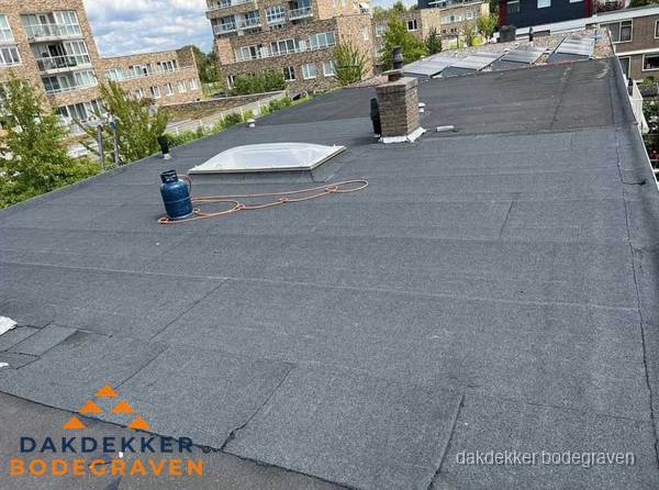 Bitumen dakbedekking op plat dak met lichtkoepel en schoorsteen in Bodegraven